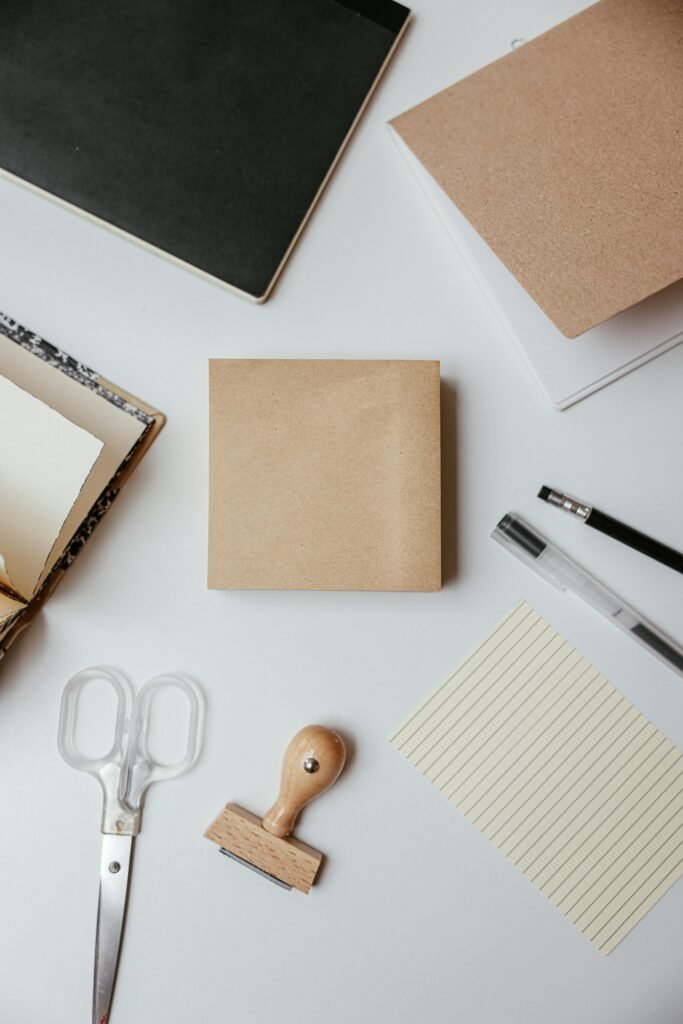 Flat lay of stationery items including notepad, pens, and scissors on a white desk.